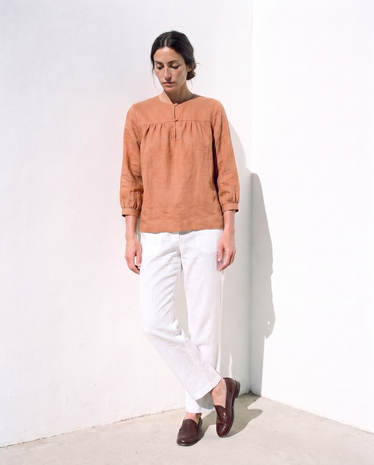 Ines Blouse in clay, leaning against a sunlit wall