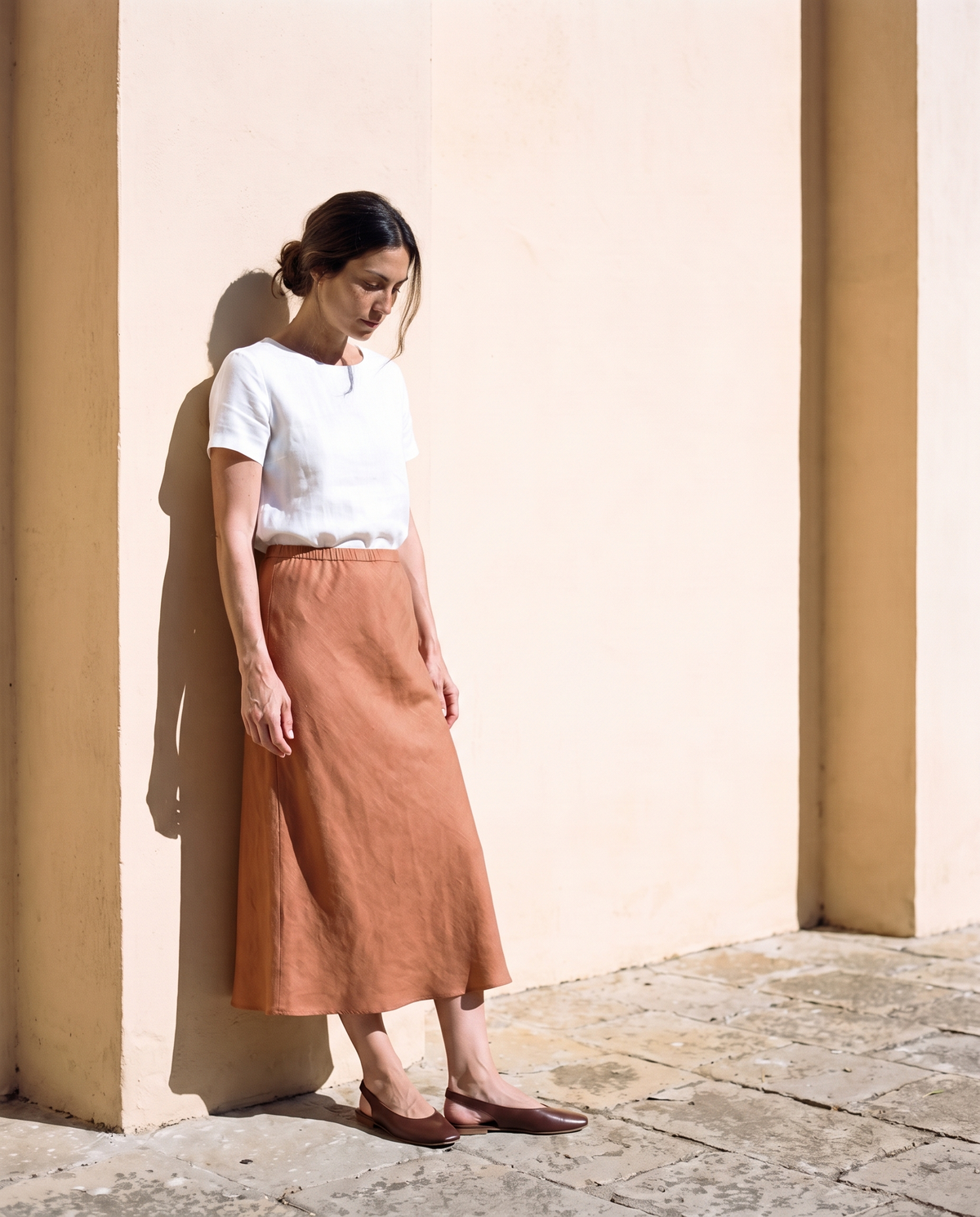 Marta Slip Skirt in clay, leaning against a sunlit wall