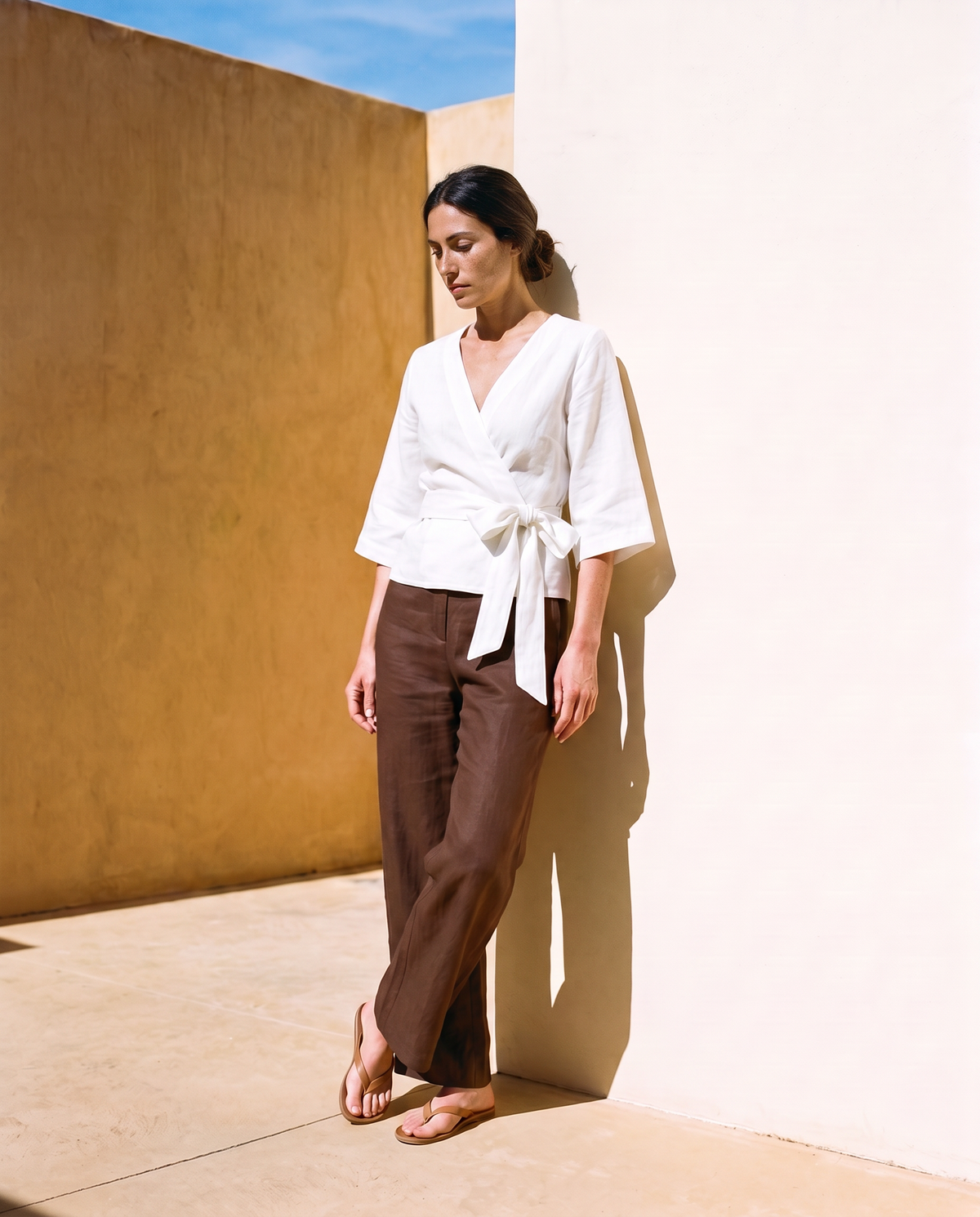 Lucia Wrap Top in white, leaning against a sunlit wall