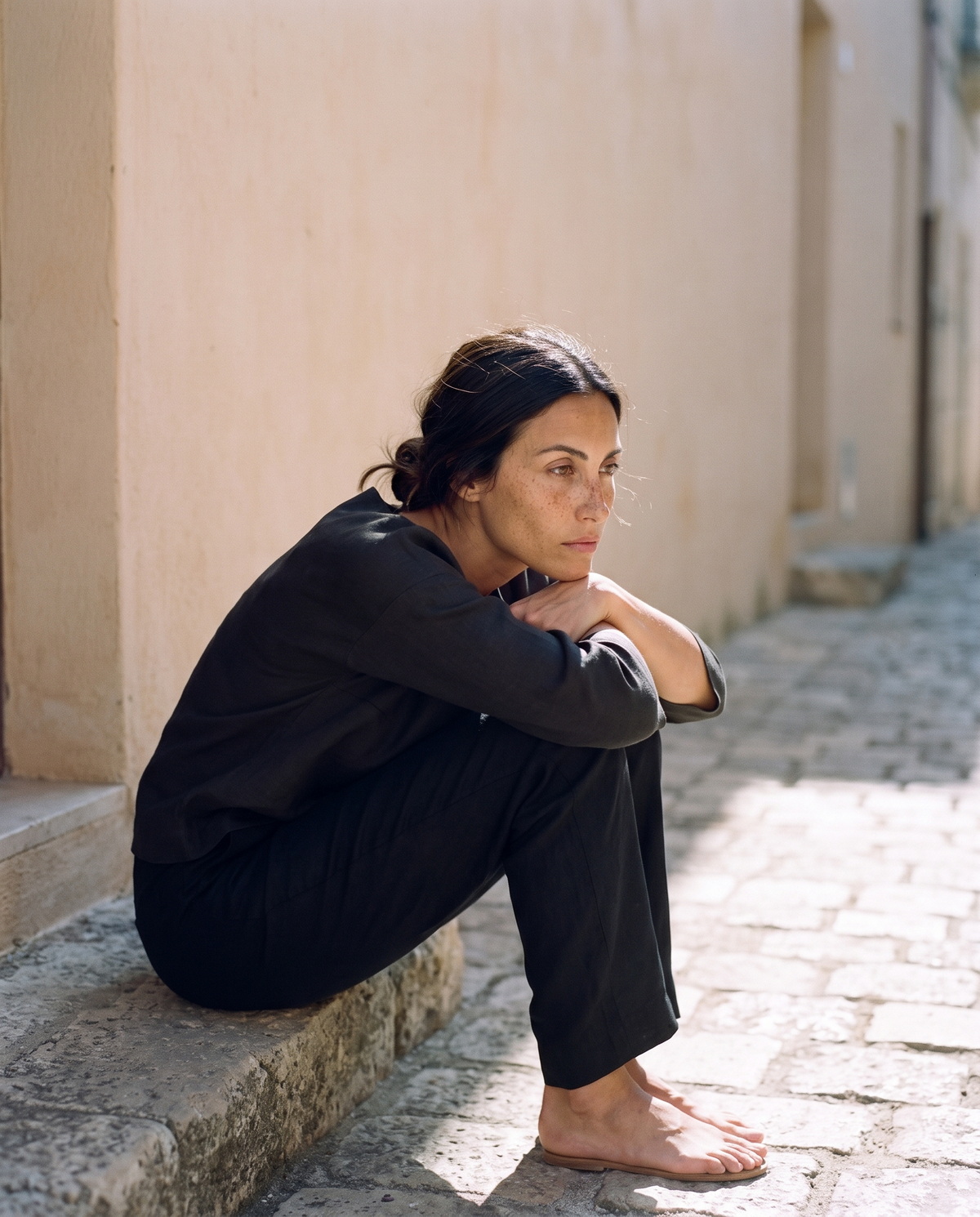 Black boxy top and straight leg trouser set, sitting on a stone step in the shade