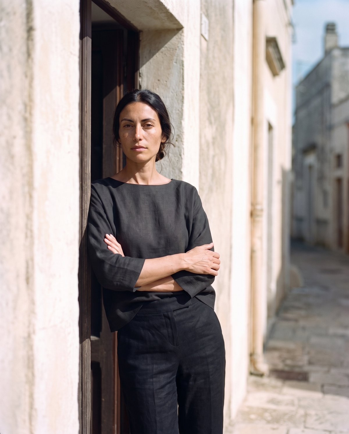 Black boxy top and straight leg trouser set, arms folded in a doorway looking down the lane