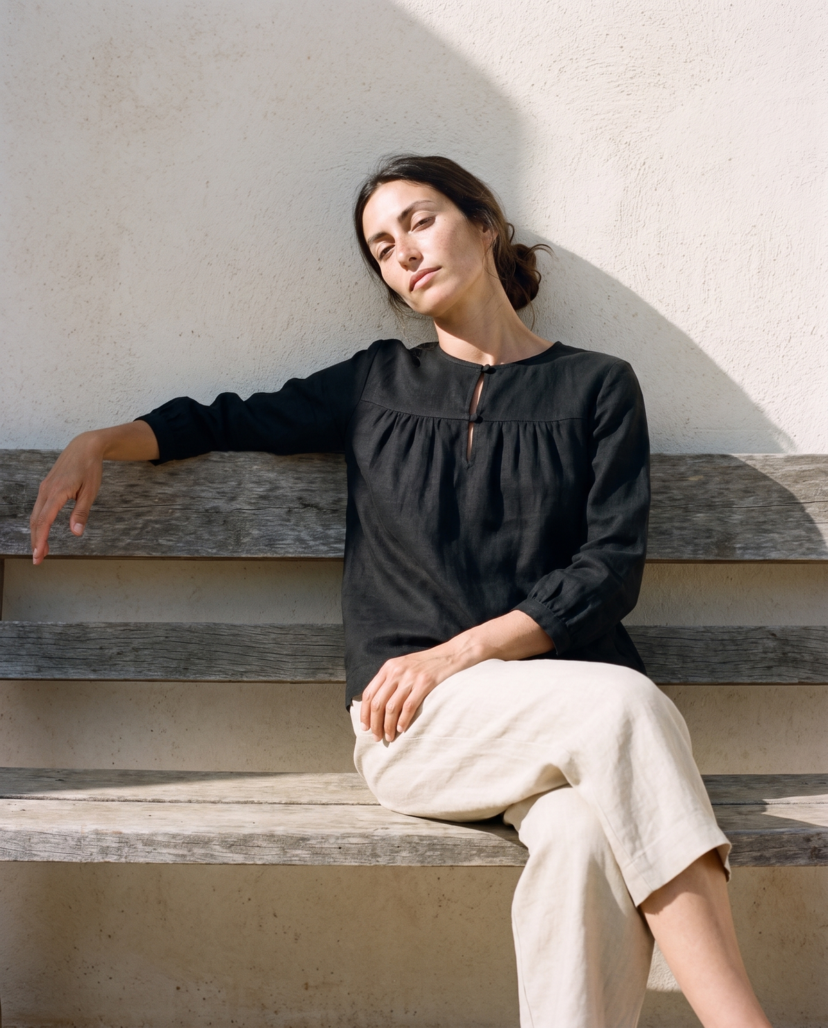 Black gathered yoke linen blouse and natural culottes, resting on a wooden bench against a wall
