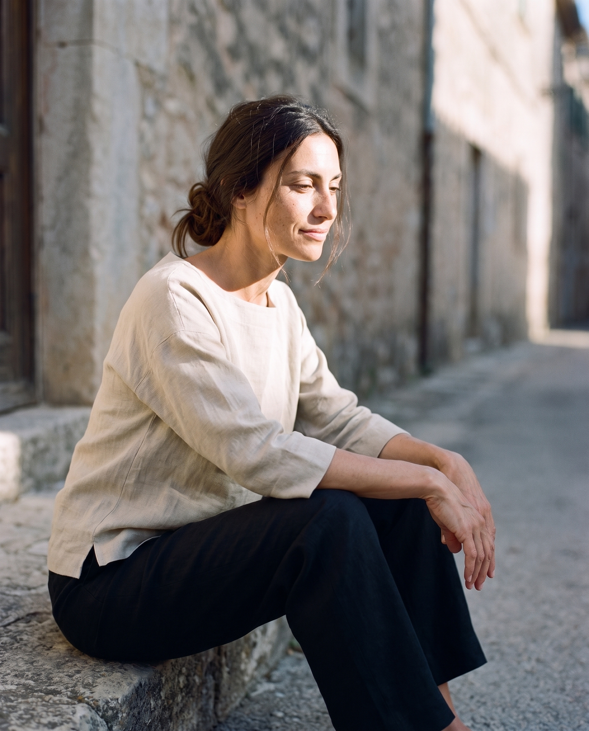 Natural boxy linen top and black straight leg trousers, sitting on a doorstep looking down an empty lane