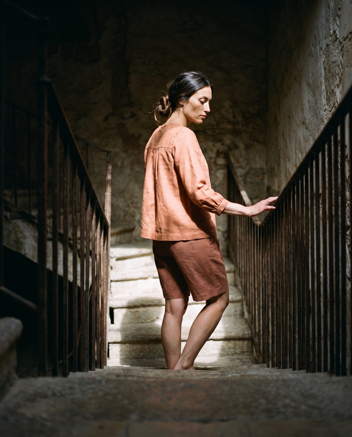 Clay yoke blouse and Bermuda shorts set, climbing a stone staircase with a hand on the rail